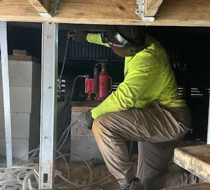 A man in a yellow shirt constructs a wooden structure, focused on his task in a well-lit environment.